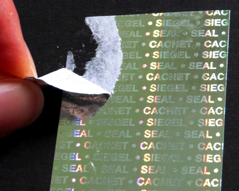 Silber glänzendes Hologrammpapier mit Siegel Seal Cachet zerreißt beim Ablösen