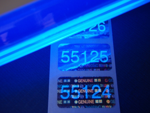Spezielles UV-Licht macht die zuvor quasi unsichtbare Sicherheitsnummerierung auf Hologrammetiketten sichtbar