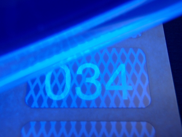 Die Sicherheits-Nummerierung auf silberner Rautenmusterfolie ist erst unter blauem UV-Licht sichtbar