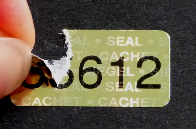Siegel aus goldenem Hologrammpapier mit Nummerierung zerreißen bei Ablöseversuchen